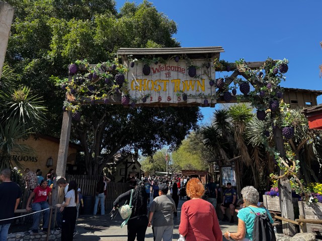 Entrance sign to Ghost Town at Knott's Berry Farm, adorned with grape decorations and surrounded by visitors.